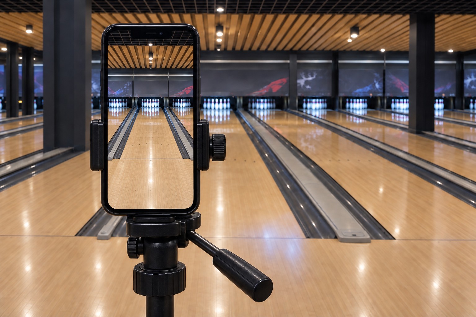 Close view of a phone secured vertically in a tripod clamp. The preview centres one bowling lane with both gutters and the white pins visible.