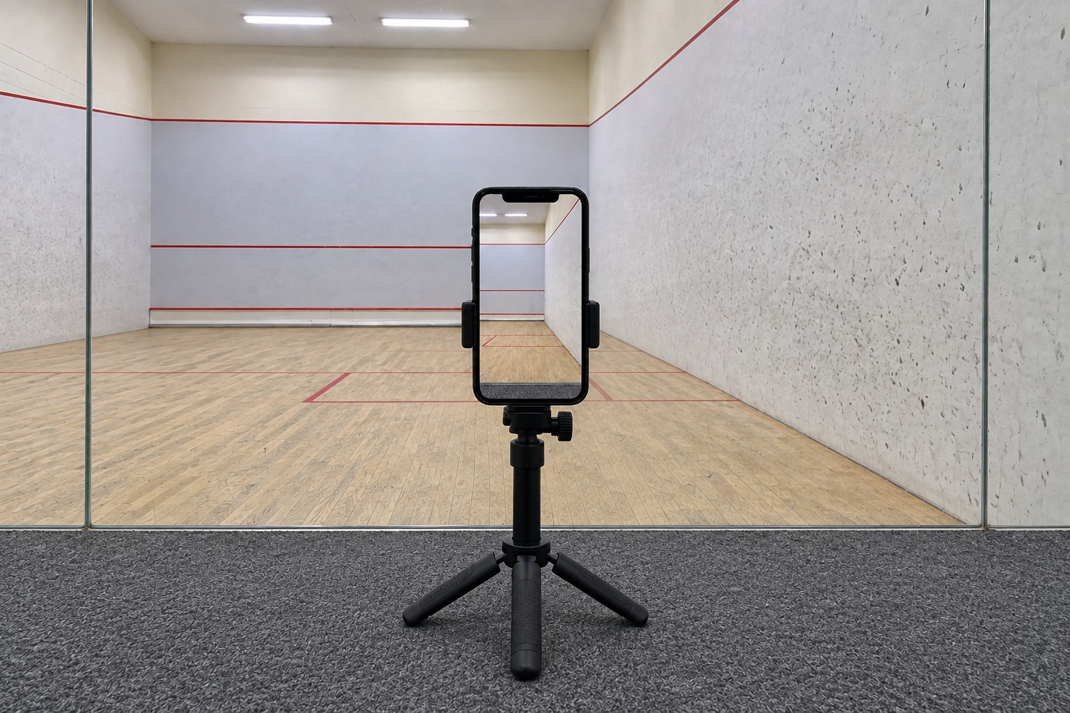 Full tripod outside the rear glass, aligned straight toward the right-side squash court.